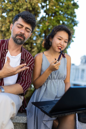 Two colleagues engaged in a friendly outdoor discussion while working on a laptop, capturing a moment of collaboration and communication in a natural settingの写真素材