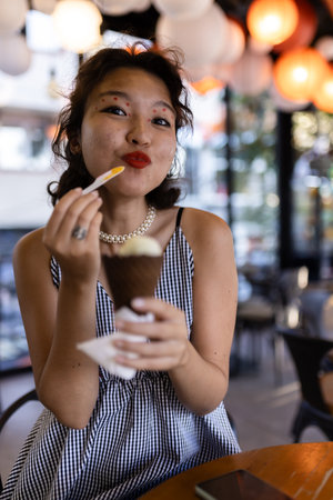 Young woman enjoying ice cream cone in a vibrant cafe with colorful decorationsの写真素材