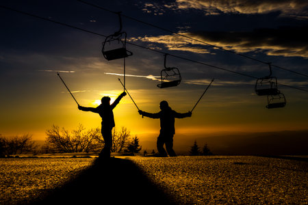 Two skiers silhouetted against a stunning sunset sharing an enthusiastic high fiveの写真素材