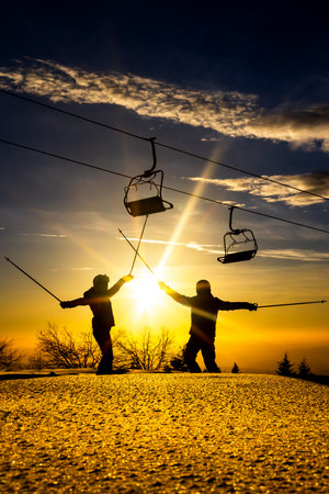 Skiers enjoying a sunset on the slopes, silhouettes against the golden skyの写真素材