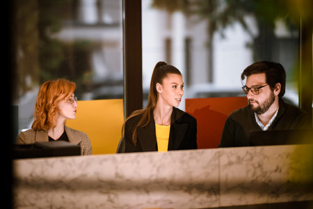 Three young adults engaged in a discussion at a modern office space during daytime with bright colors in the backgroundの写真素材