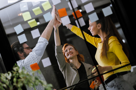 Team collaboration is celebrated with high fives and sticky notes in a bright office during a brainstorming session in the afternoonの写真素材
