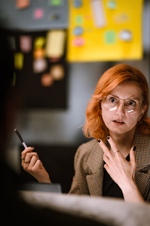 Woman with orange hair discusses ideas in a creative workspace filled with colorful notes and sticky paper during a collaborative session in the afternoonの写真素材