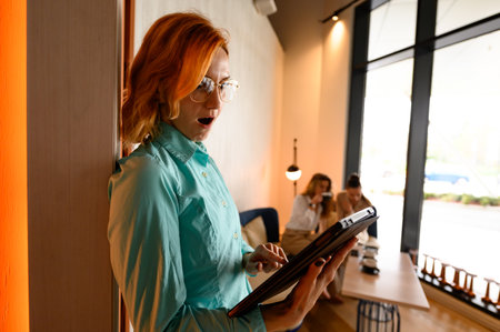 Businesswoman engaging with a tablet while expressing surprise in a modern coworking space during...