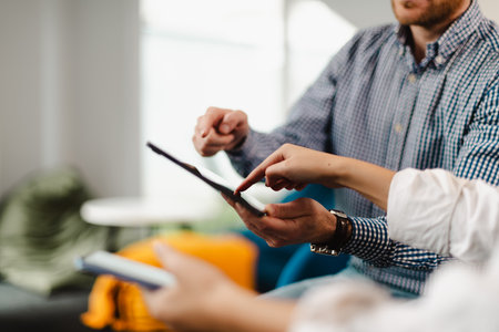 Business professionals collaborate over a digital device in a modern office setting while discussing strategies and sharing insights in an informal meetingの写真素材