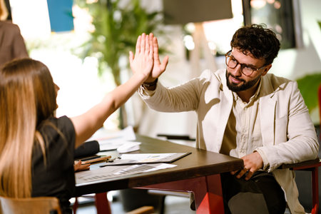Business meeting between two professionals with a friendly high-five in a modern office setting during the dayの写真素材