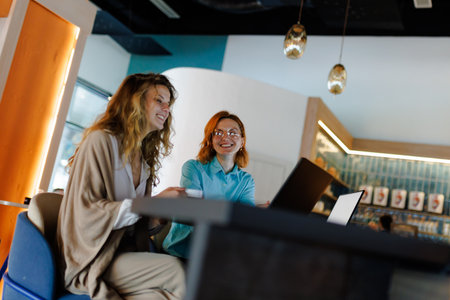 Businesswomen collaborate in modern workspace, engaging with technology and ideas during a productive meeting in a stylish cafeの写真素材
