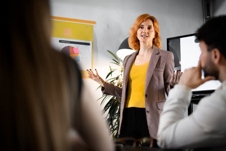 Business presentation by a woman in a stylish outfit at a modern office setting with engaged audience members in the backgroundの写真素材