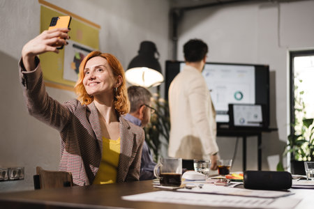 Business meeting with focused discussions and a smiling participant taking a selfie in a modern office environmentの写真素材