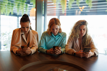 Businesswomen engaged in group discussion while using smartphones in a modern office environment during daytimeの写真素材