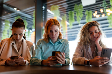 Businesswomen engage with smartphones while collaborating in a modern office space during a late afternoon meetingの写真素材