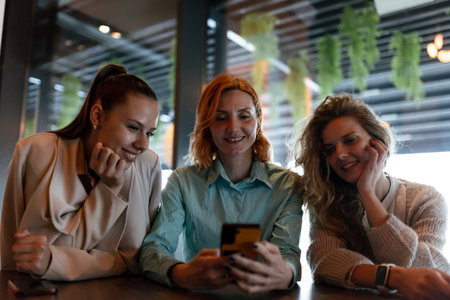Three businesswomen engaged in a discussion over a smartphone at a modern workspace during a bright afternoonの写真素材