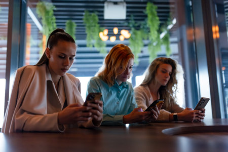Businesswomen engaged in mobile communication at a stylish cafe during a networking event in an urban settingの写真素材