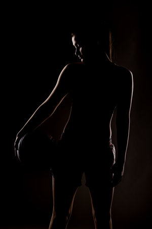 Silhouette of a young female basketball player holding a ball, dramatic lighting in studio backgroundの写真素材