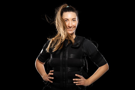 Woman in an EMS fitness suit with electrodes, smiling confidently during a high-tech workout session showcasing strength, training technology, and modern fitness apparelの写真素材