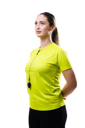 Athletic woman in neon yellow sports shirt with whistle stands confidently on a white background, ready for training, coaching, fitness session, or outdoor sports.の写真素材