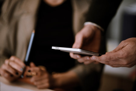 Meeting in a modern office with a man handing a smartphone to a colleague while a woman observes,...
