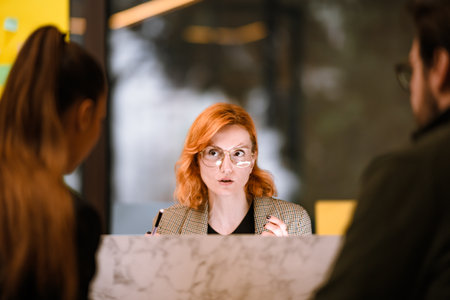 Professional woman with orange hair engaged in discussion with two individuals at a modern office...