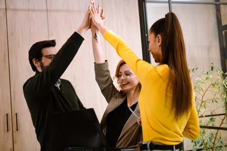 Team members celebrate success in a modern office setting during a meeting, showcasing joy and...