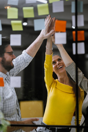 Team members celebrate successful brainstorming session in a modern office with colorful sticky...