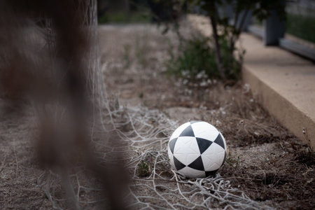 Soccer ball resting on dusty ground among tangled netting in an outdoor setting, capturing a quiet moment of sport and neglectの写真素材