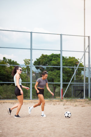 Two women play soccer on an outdoor field, sharing laughter and teamwork under a sunny skyの写真素材