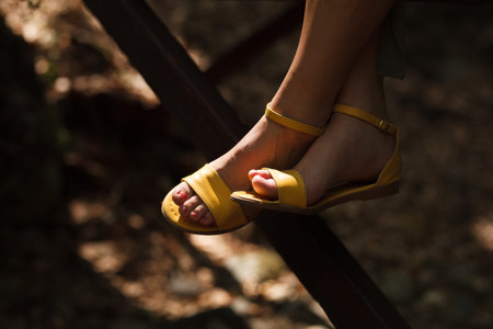 Elegant yellow sandals resting on a wooden railing amidst natural surroundings, showcasing a relaxed...