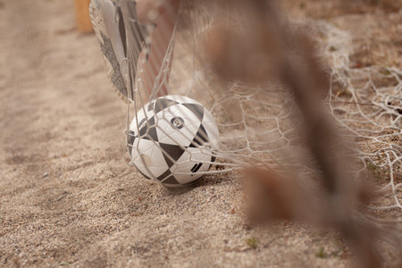 A soccer ball is tangled in a beach net on a sandy shore, capturing a dramatic close-up of outdoor...