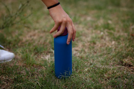 Hand reaching for a blue water bottle on grass during a badminton practice session in a sunny outdoor fieldの写真素材