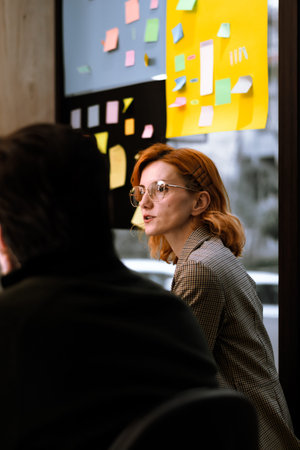 Creative brainstorming session taking place in a modern office with a woman wearing glasses and...