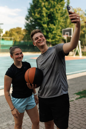 Two basketball players enjoying a sunny day on the court while taking a selfie with a basketball in hand, capturing joyful moments of camaraderie and funの写真素材