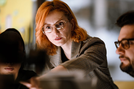Meeting in a modern workspace with a woman guiding colleagues on a project while discussing ideas and solutions during a brainstorming sessionの写真素材