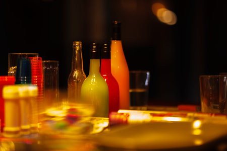 Bottles and glasses arranged on a table in low lighting with a warm ambianceの写真素材