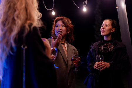 Three women enjoying an evening conversation outdoors at a gatheringの写真素材