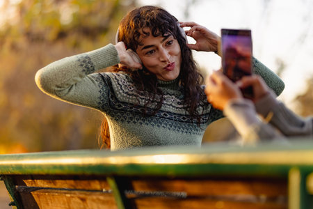 Playful young woman poses for a photo with a friend in a park during sunset, wearing a cozy sweater and enjoying the fresh air and natureの写真素材