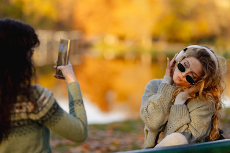 Two friends enjoy a sunny afternoon by the lake while one takes a picture and the other poses with sunglassesの写真素材