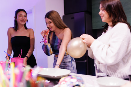 Three women celebrating together with balloons and party toys in a festive indoor settingの写真素材