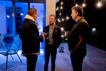 Three friends enjoying a casual evening gathering with drinks and outdoor lighting under clear night skies, creating a warm and relaxed social atmosphere.の写真素材