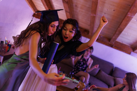 Young women celebrating graduation with friends, taking selfies and enjoying a festive party atmosphereの写真素材