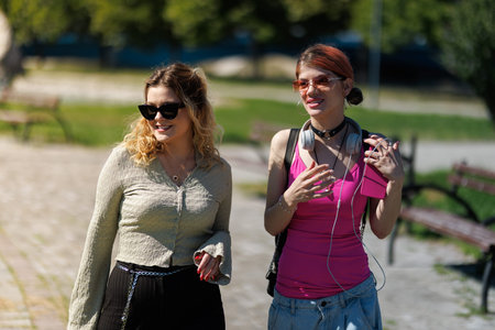 Girls walk and talk in a park while enjoying a sunny day and wearing casual clothes during the afternoon hoursの写真素材