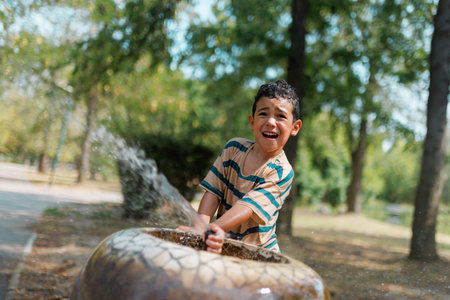Young boy enjoying water splash from a park fountain on a sunny dayの写真素材