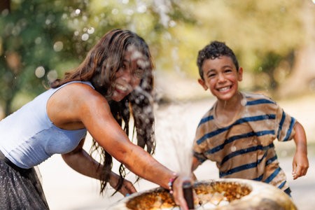 Joyful moments with a woman and a boy playing at a water fountain in a sunny outdoor park