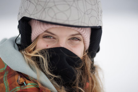 Girl wearing a helmet and mask smiles while enjoying winter activities in the snow during a bright...