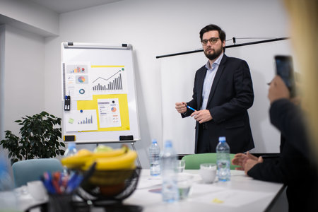 Business meeting in an office where a man presents data and charts while others listen and take...