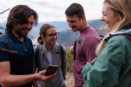 Group of friends laughing and checking a phone during a hiking trip on a mountain trail