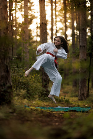 Girl practices karate moves in a lush forest setting during late afternoon light with trees surrounding her