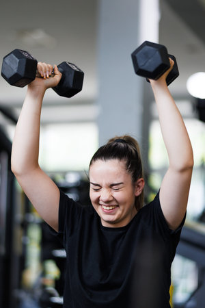 Young woman lifts dumbbells in a gym during a workout session focusing on strength training and fitness in the morning hours with equipment around her