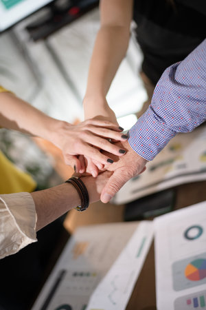 Business team collaborates during a meeting by joining hands over a table filled with charts and reports in a modern office setting in the afternoon