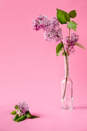 pink background with lilac flowers in elegant glass bottle. greeting card, invitation card. Color. Place for textの写真素材