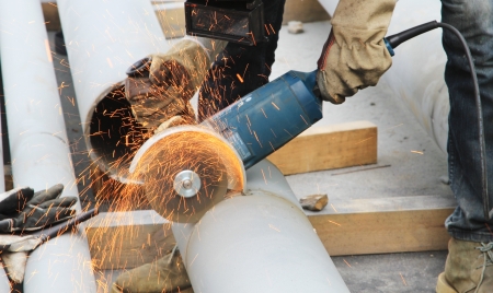 Worker cut steel pipe by grinder, working place background.